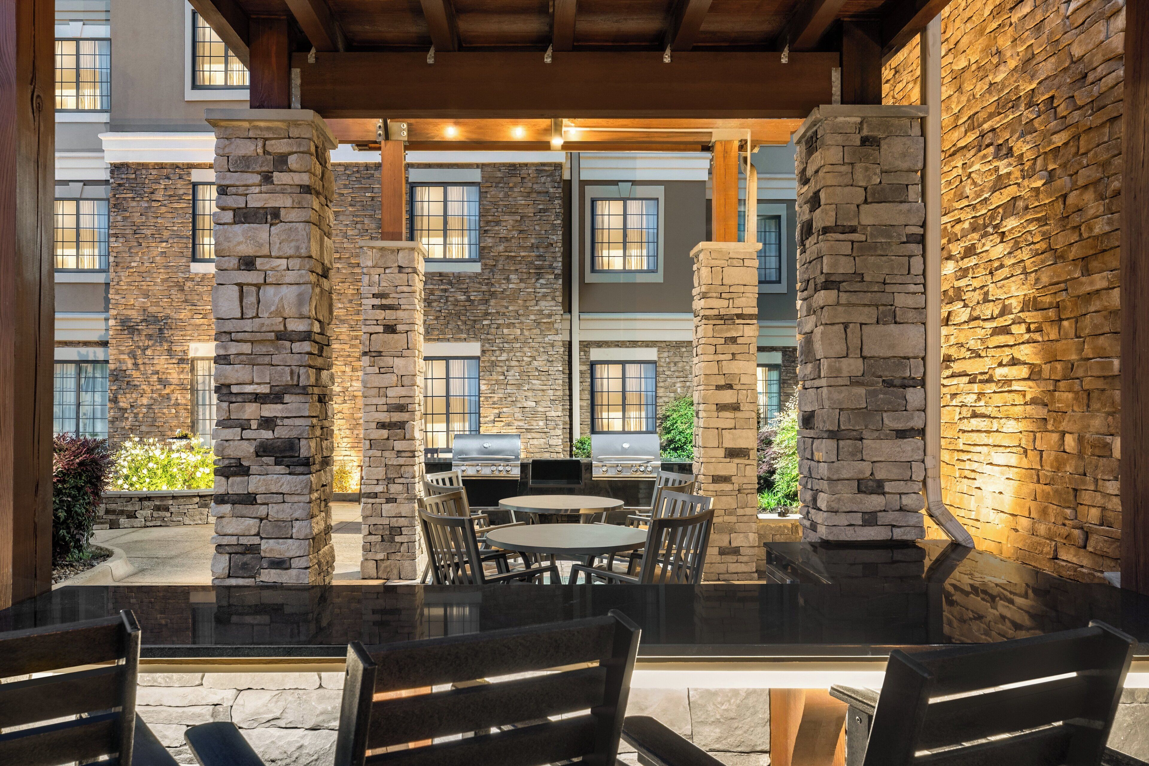 An outdoor patio area with stone pillars, a grill, and a round table with chairs.