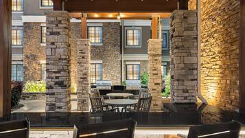 An outdoor patio area with stone pillars, a grill, and a round table with chairs.