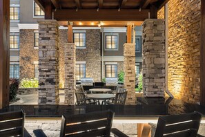 An outdoor patio area with stone pillars, a grill, and a round table with chairs.