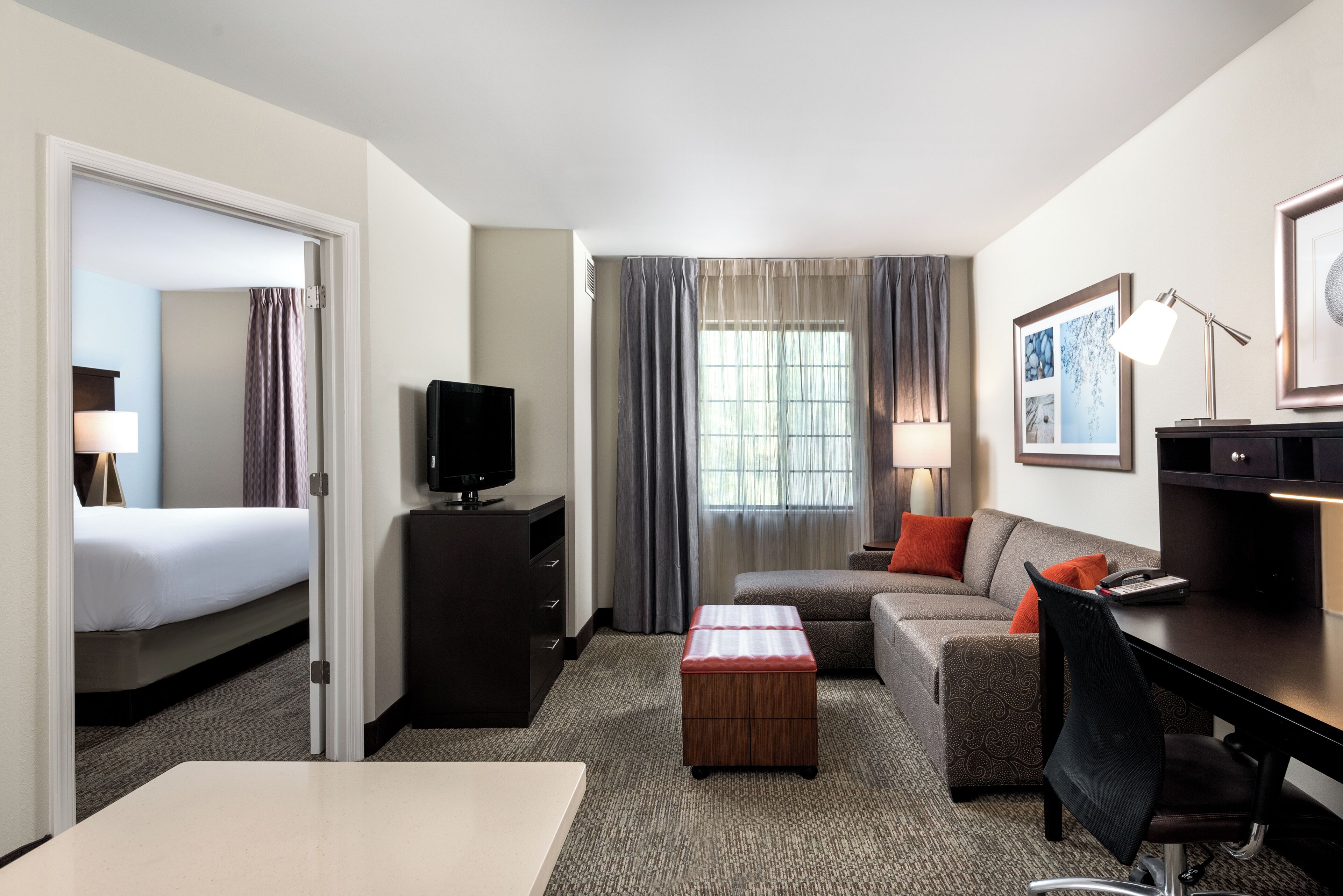 A hotel room with a bed, a desk, a television, a sofa, a chair, a small table, and a window with curtains.