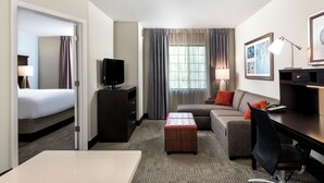 Ein Hotelzimmer mit Bett, Schreibtisch, Stuhl, Fernseher, Lampe und einem Fenster mit Vorhängen.