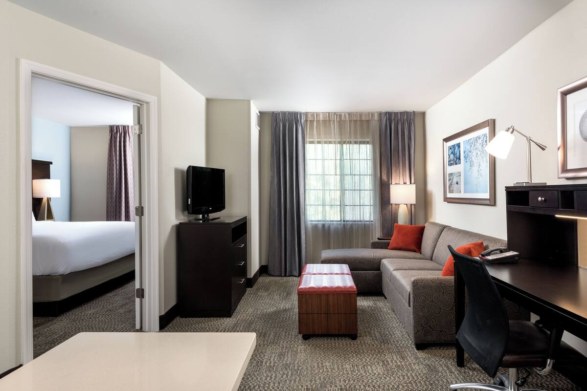 A hotel room with a bed, a desk, a chair, a TV, a lamp, and a window with curtains.