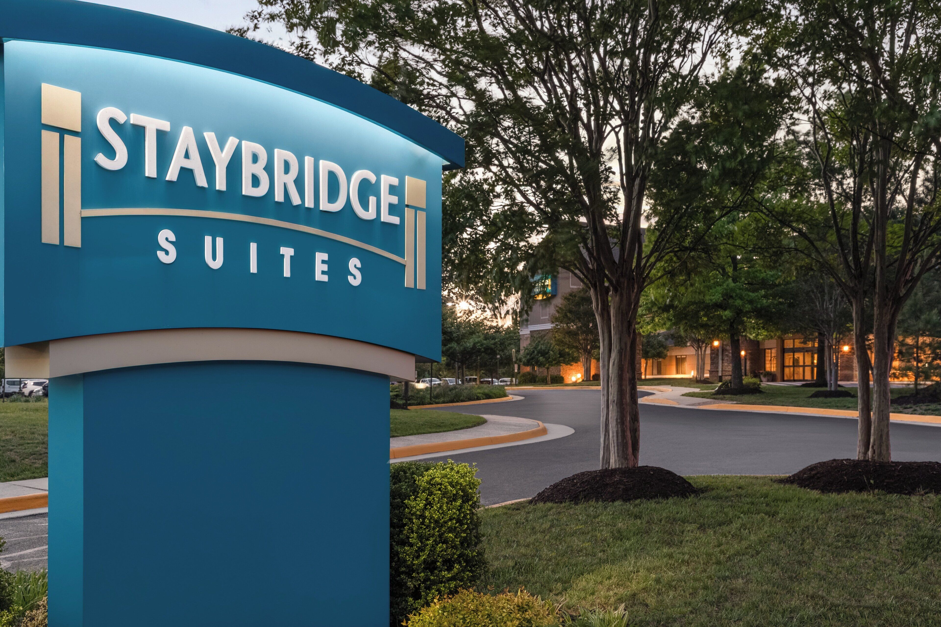 A sign for Staybridge Suites with a curved design and the name prominently displayed.