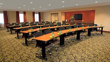 A conference room with multiple tables, chairs, and a television screen on the wall.