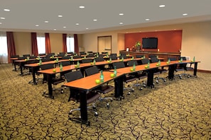 A conference room with multiple tables, chairs, and a television screen on the wall.