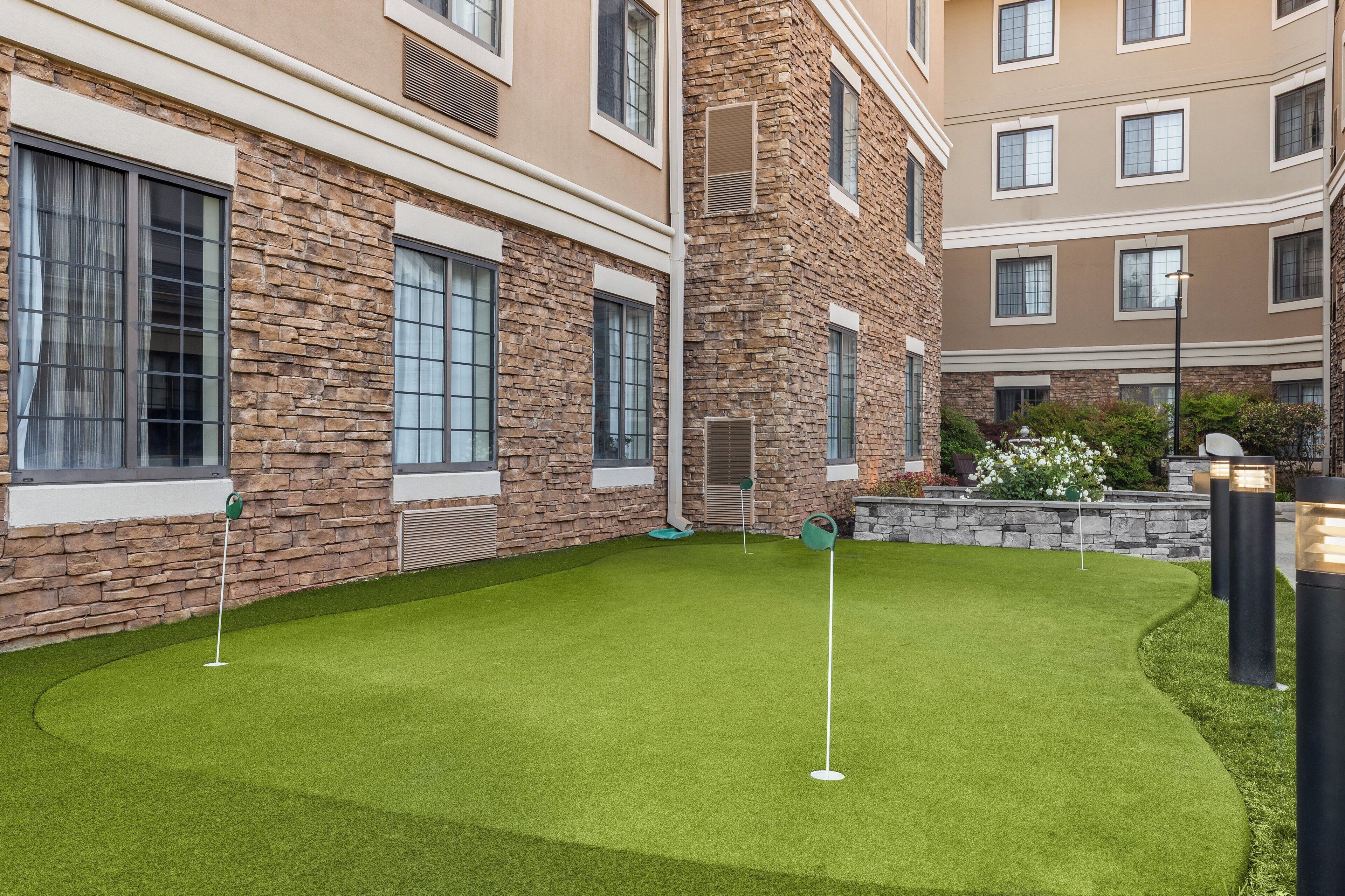 Un patio con césped artificial, un putting green y fachadas de edificios de piedra y ladrillo.