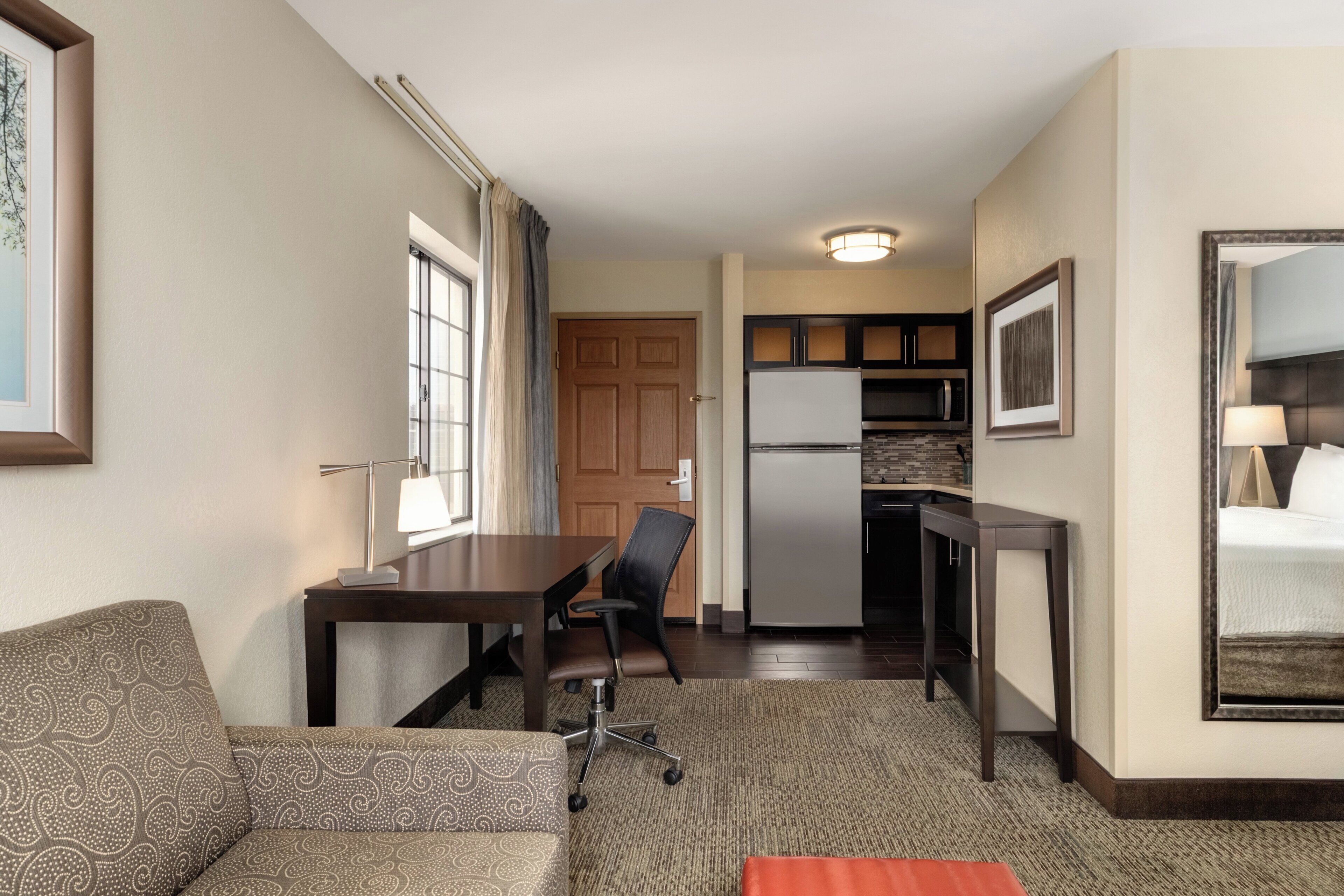 Une chambre d’hôtel compacte comprenant un canapé, une petite table à manger, une chaise, un coin cuisine et un grand miroir.