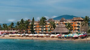 Ein Strandresort mit mehreren Gebäuden, Palmen und Strandliegen.