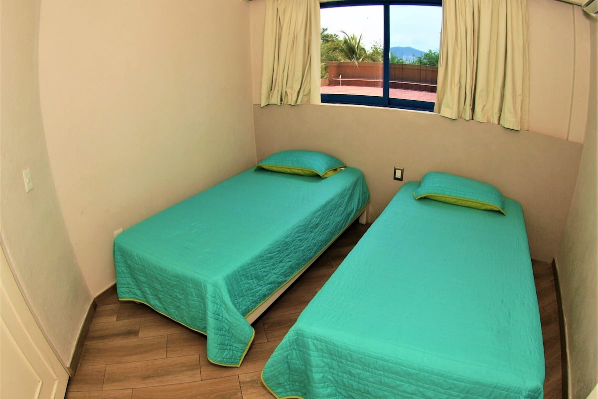 Una habitación pequeña con dos camas individuales, una ventana con cortinas y suelo de madera.