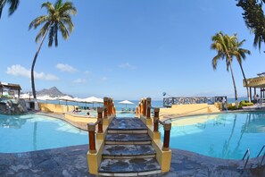 A pool area with a staircase leading to a beach, surrounded by palm trees and umbrellas. - Hotel Marina Puerto Dorado (Manzanillo)