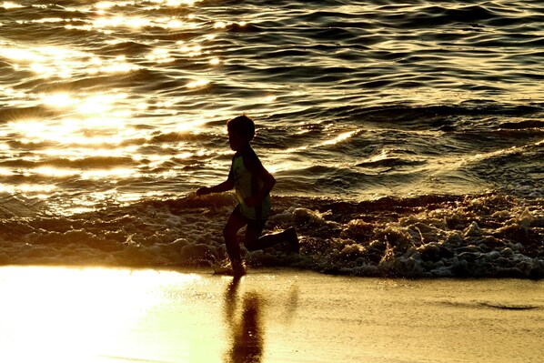 Una persona corriendo por la playa, con olas y el reflejo del sol en el agua.
