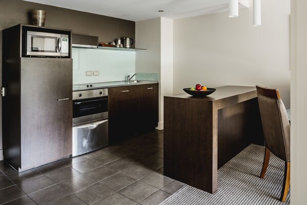 Una cocina moderna con armarios oscuros, microondas integrado y una pequeña isla con un tazón de fruta.