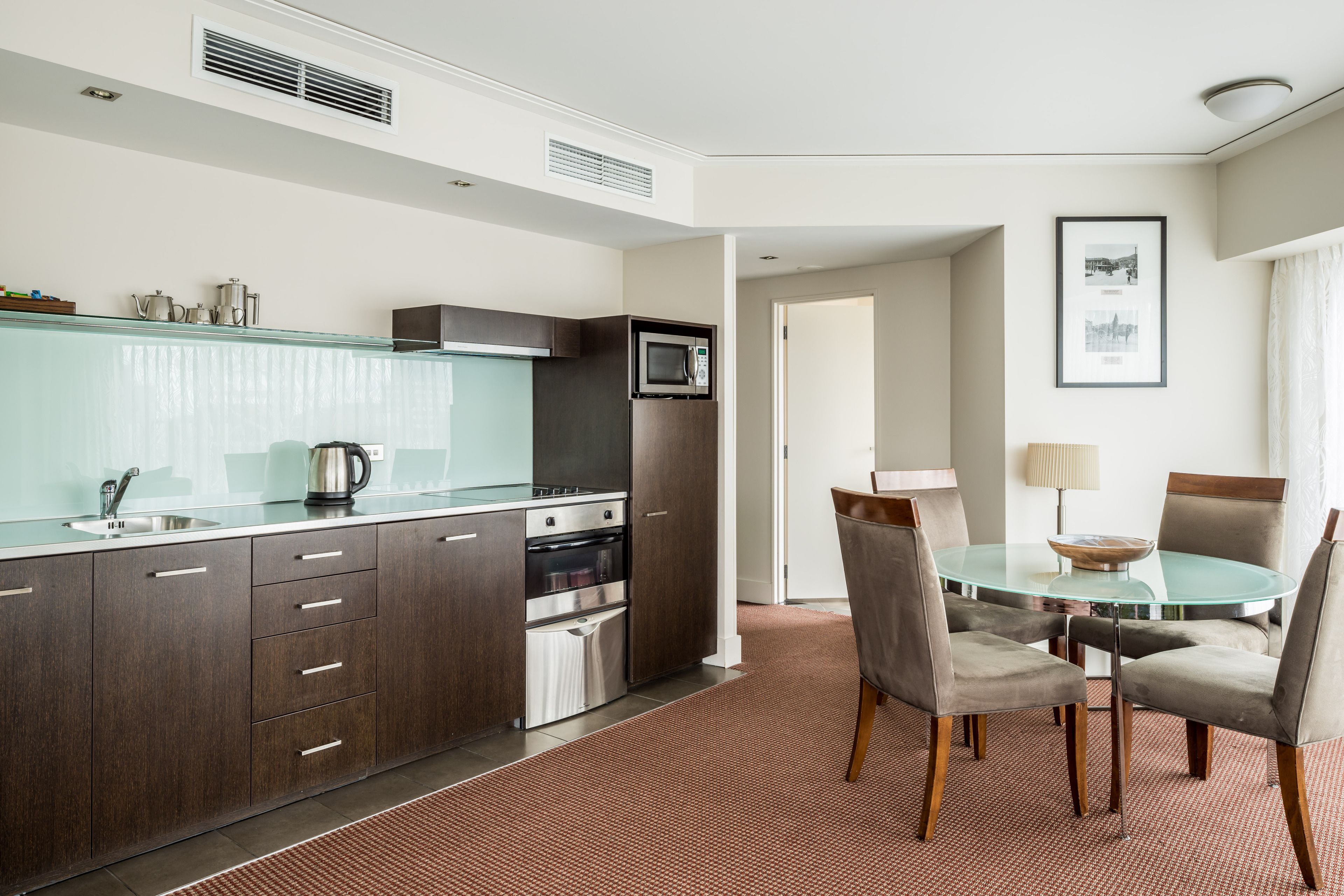 A modern kitchen with dark wood cabinets, stainless steel appliances, and a glass-top dining table with chairs.
