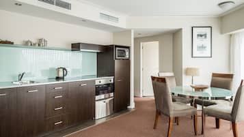 A modern kitchen with dark wood cabinets, stainless steel appliances, and a glass-top dining table with chairs.