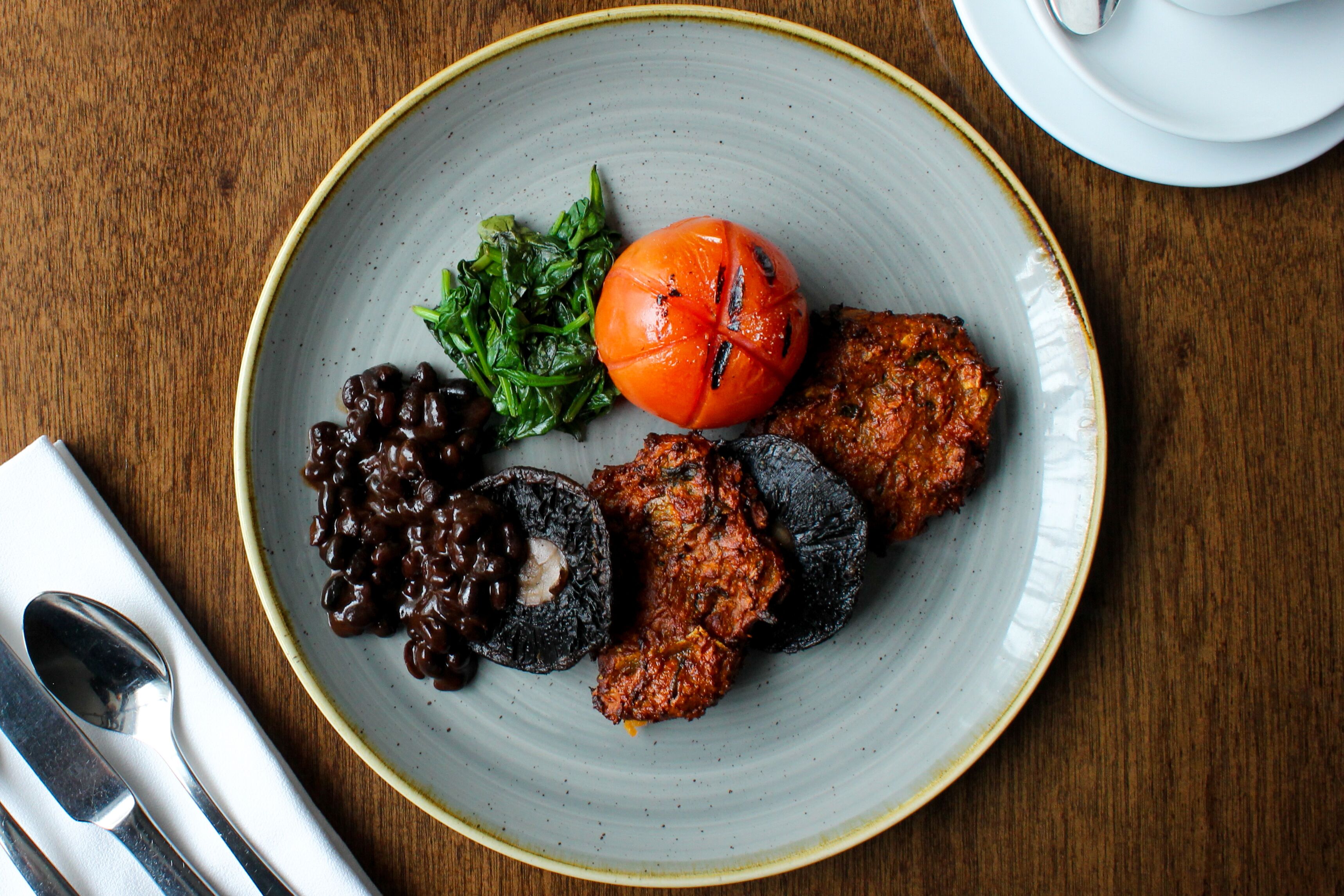 A plate with grilled meat, a tomato, and greens on a ceramic plate.