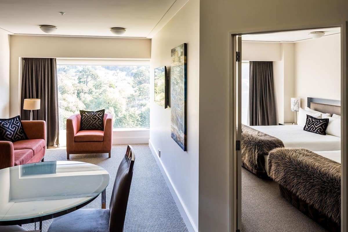Ein Hotelzimmer mit Bett, Sofa, Sessel, Tisch und Blick ins Freie.