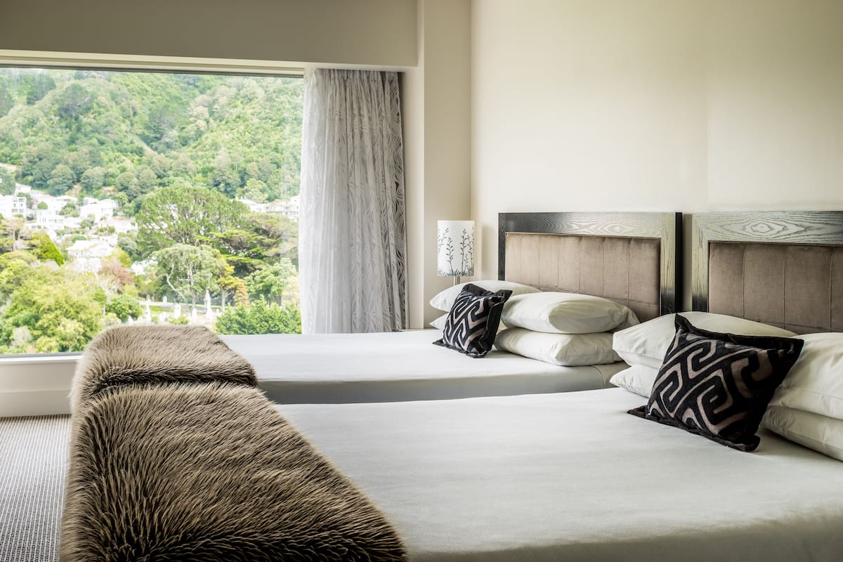 Ein Hotelzimmer mit zwei Betten, Blick auf eine bewaldete Landschaft und einem großen Fenster mit Vorhängen.
