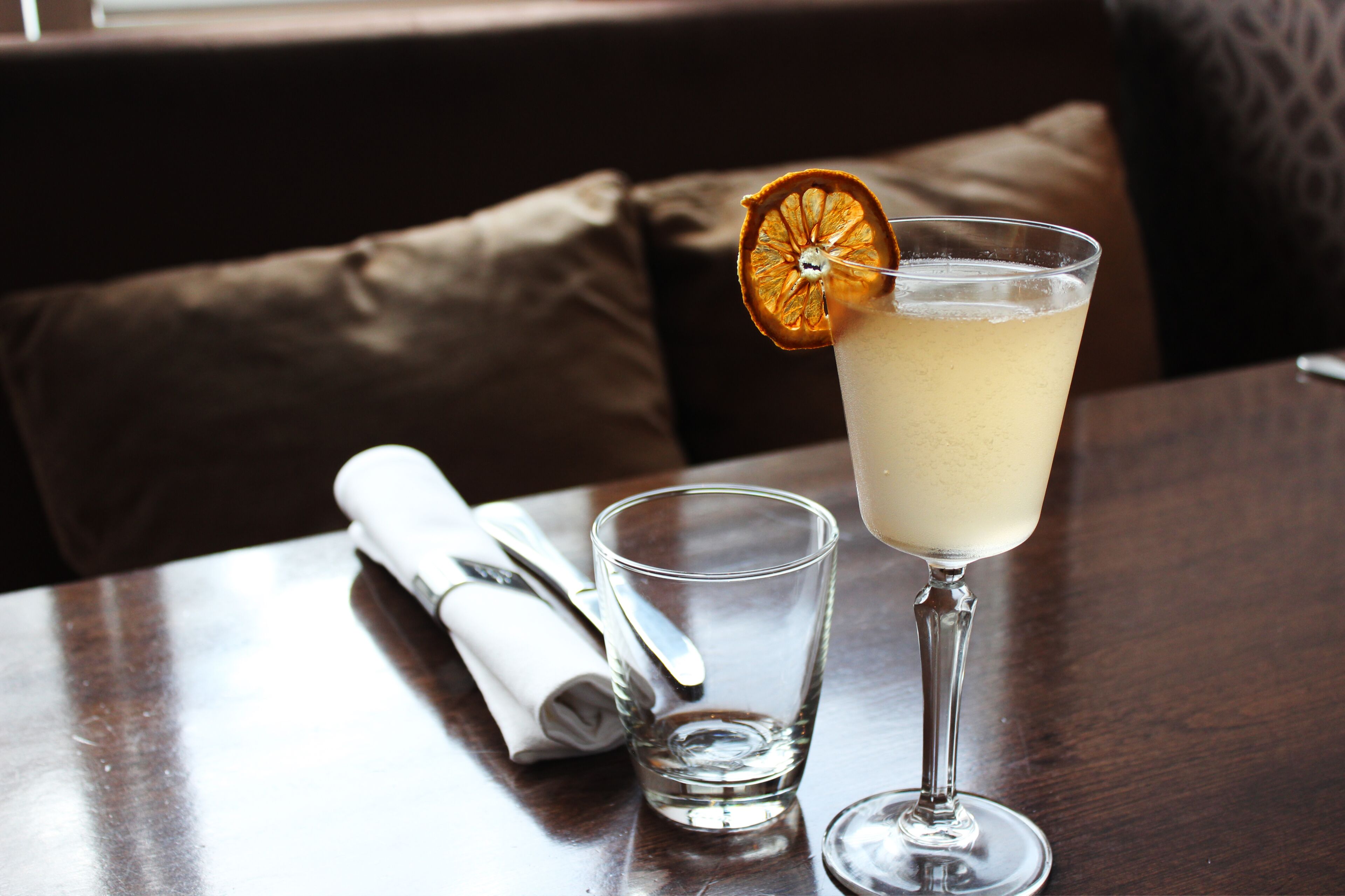 A table with a glass of a light-colored beverage, a folded napkin, and a small glass of water.