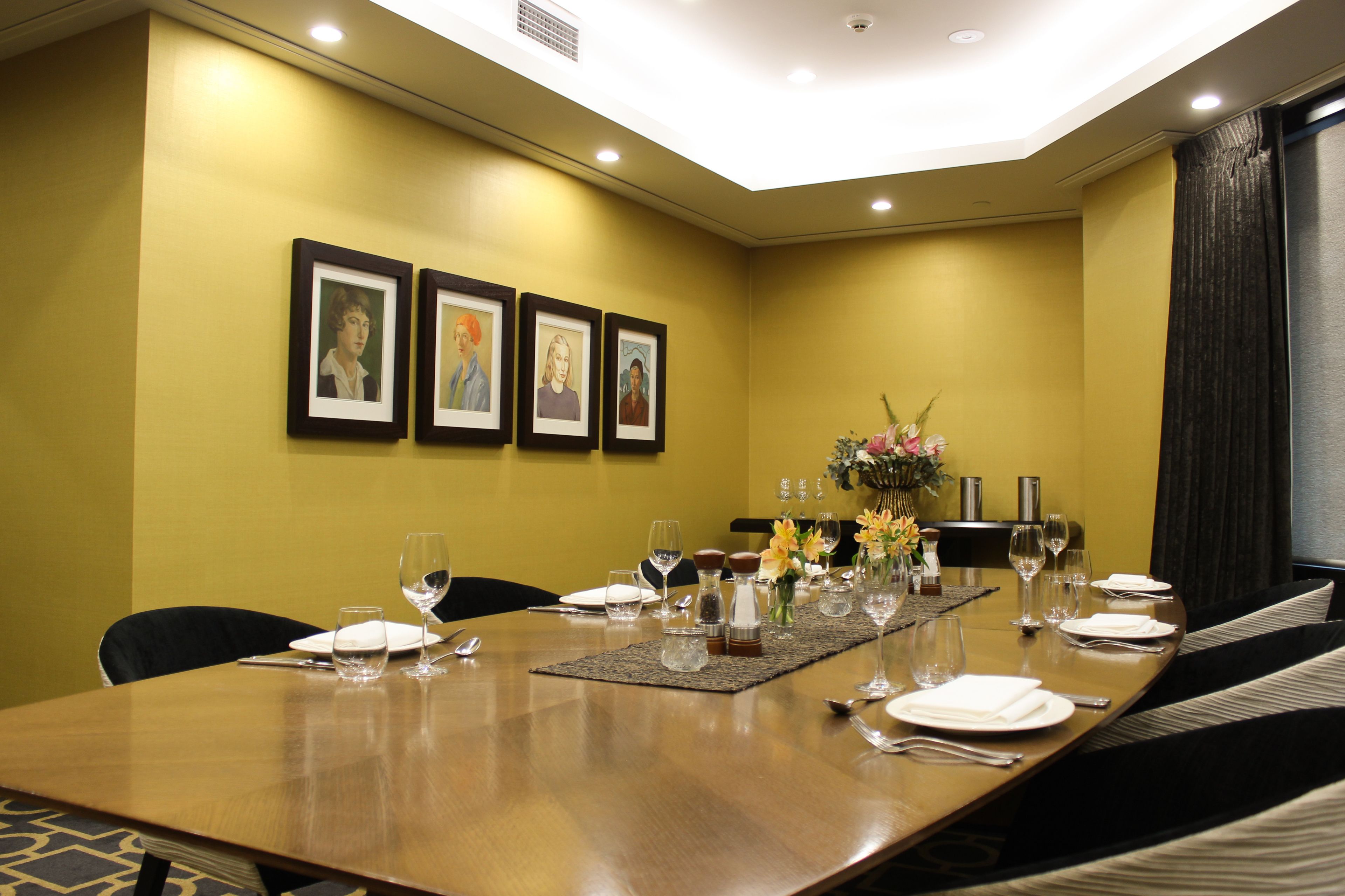 A conference room with a long table, framed artwork on the wall, and a vase with flowers.