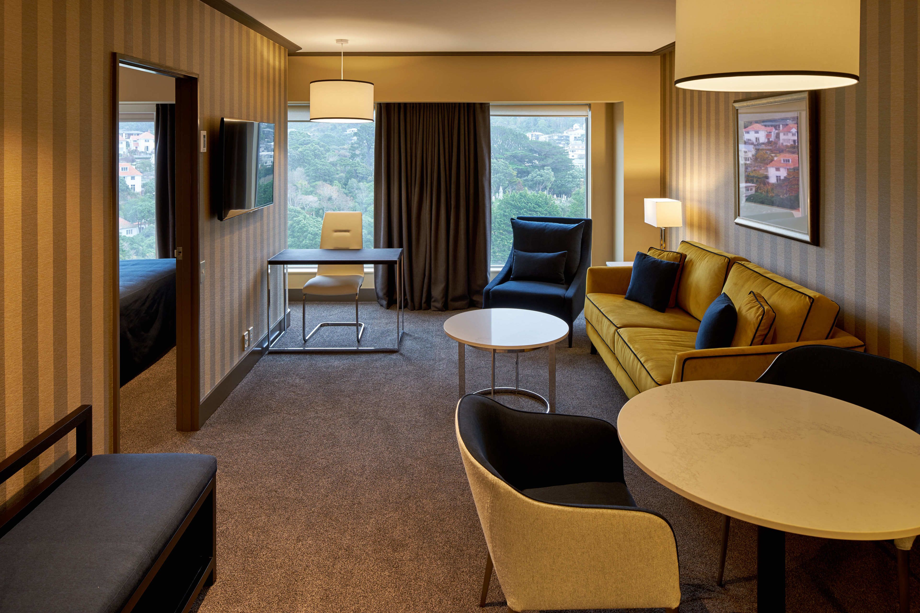 Een hotelkamer met een bed, een bank, een eettafel, een televisie en uitzicht.