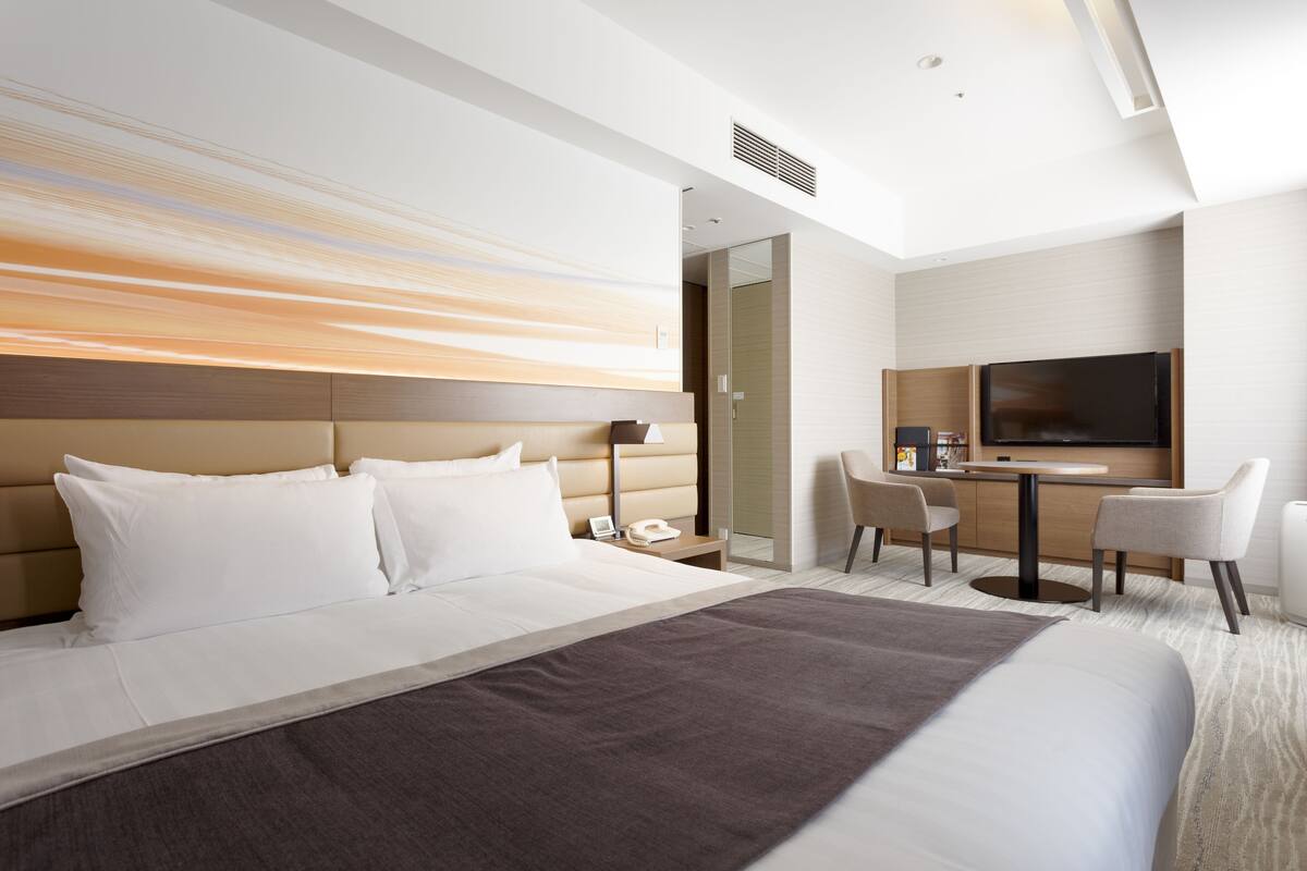 A modern hotel room with a large bed, a desk, and a TV.