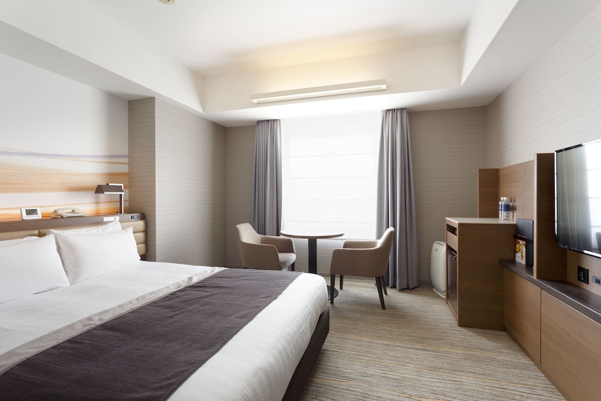 A hotel room with a bed, a desk, a chair, a television, and a window with curtains.