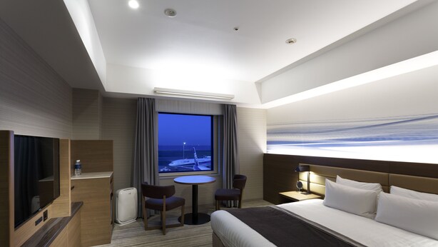 Un moderno cuarto de hotel con una cama grande, televisión, escritorio y ventana con vista al mar.