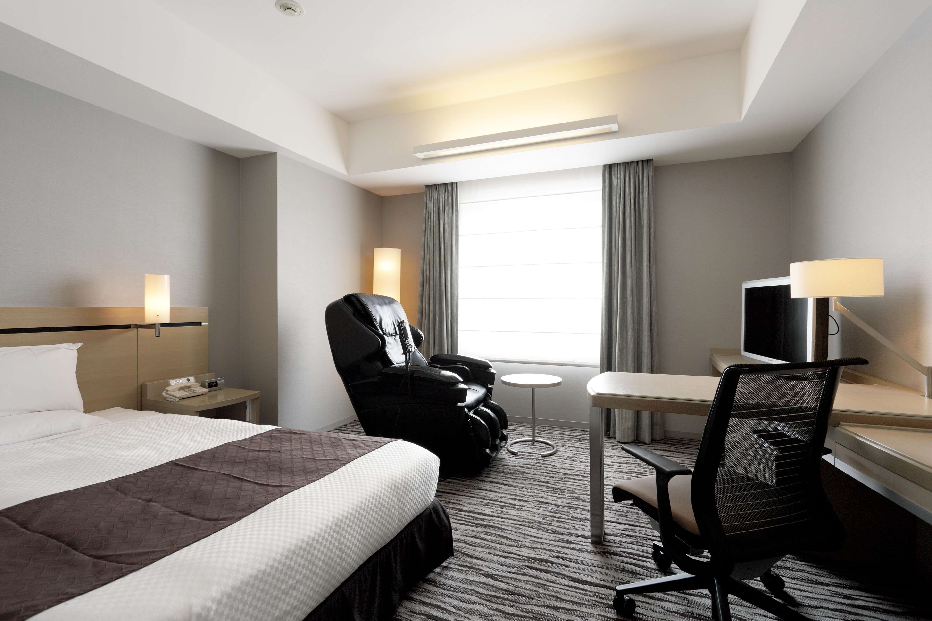 A hotel room with a bed, a massage chair, a desk, a chair, and a TV.
