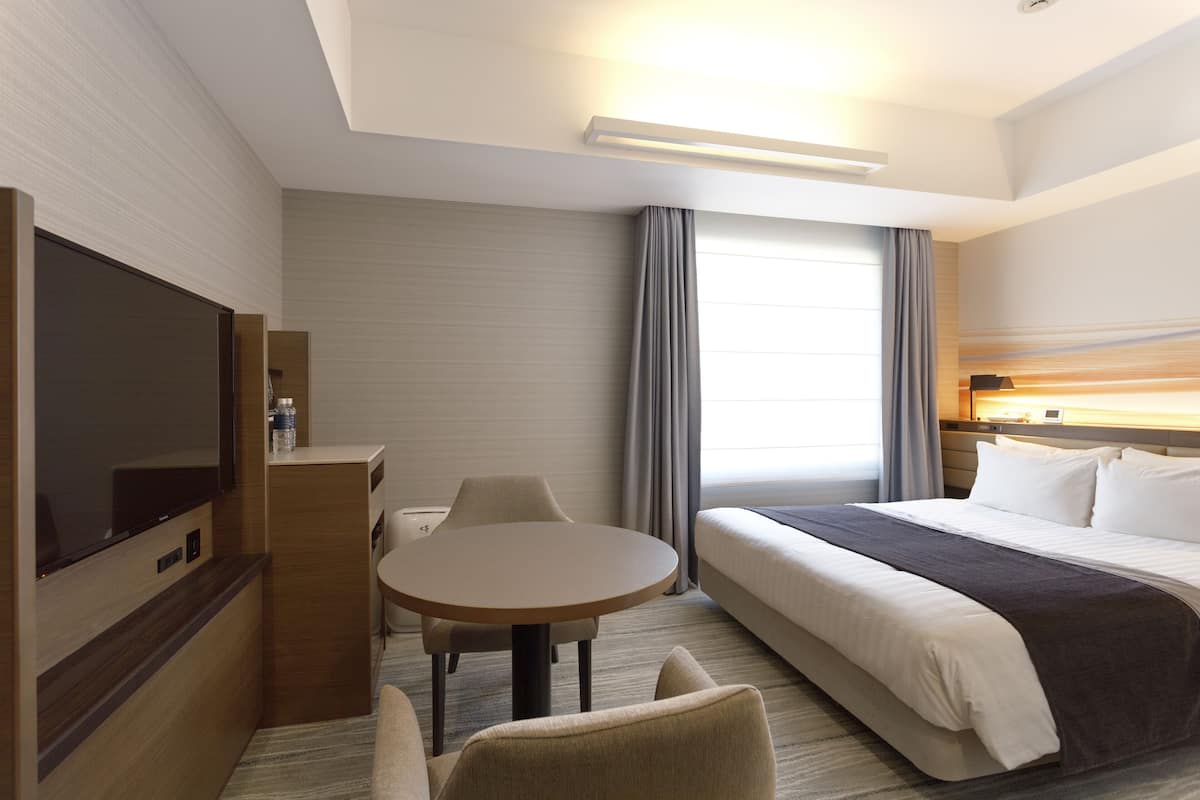 A hotel room with a bed, a TV, a desk, and a chair.