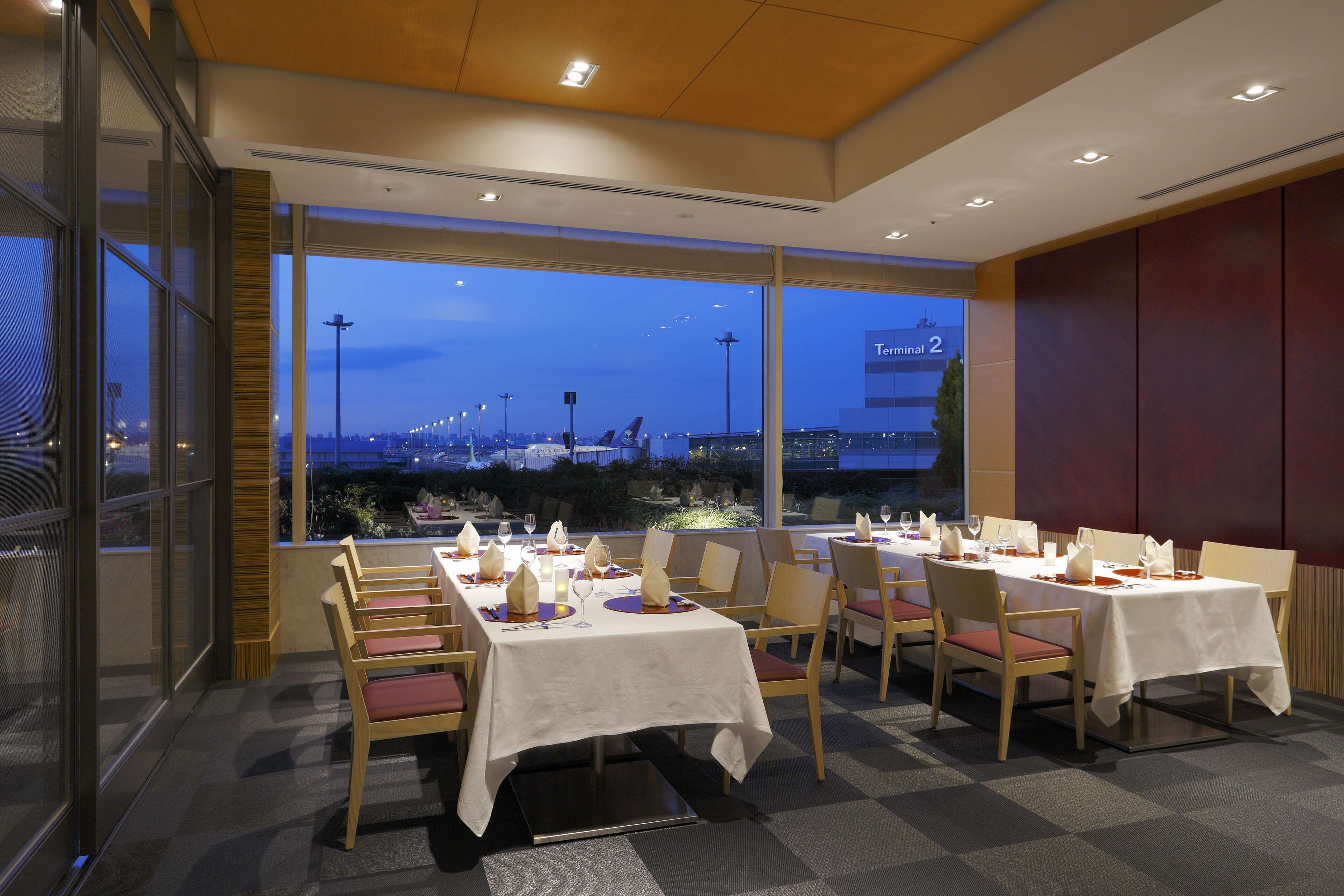 A restaurant with tables set for dining, large windows offering a view of the cityscape, and a modern interior design.