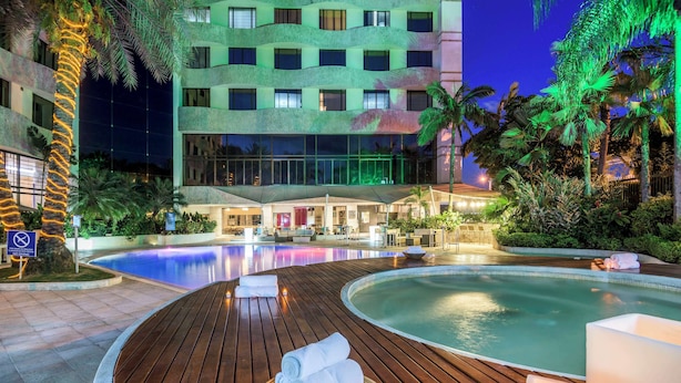 A hotel with a swimming pool, wooden deck, and lounge chairs.