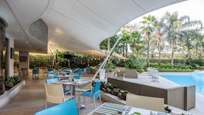 An outdoor dining area with tables and chairs, a pool, and lush greenery.
