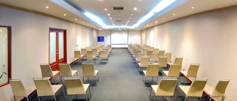 A conference room with rows of chairs, a projector screen, and a presentation screen.
