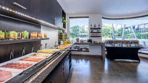 A modern buffet setup with various food items and a view of greenery outside.
