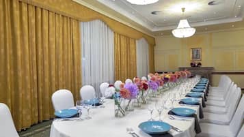 A banquet hall with round tables set for a formal event, featuring white chairs, blue tablecloths, and floral centerpieces.