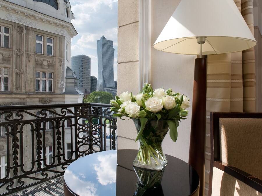 A balcony with a table, a lamp, and a vase of flowers.
