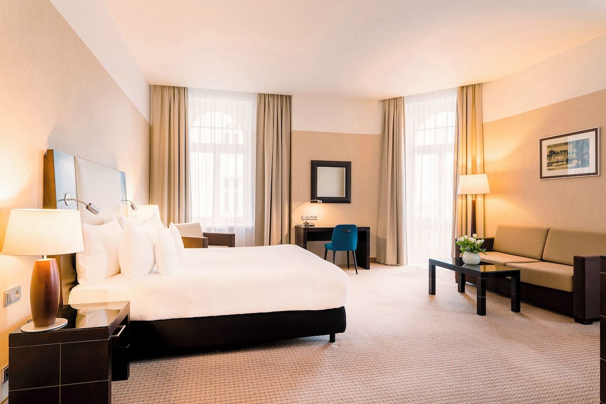 A hotel room with a large bed, a desk, a chair, a sofa, and a lamp.