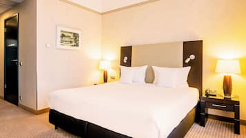A hotel room with a large bed, two bedside tables with lamps, a framed picture on the wall, and a door to the left.