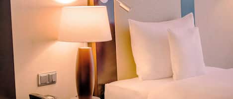Quarto de hotel com uma cama, abajur, telefone e luminária na parede.