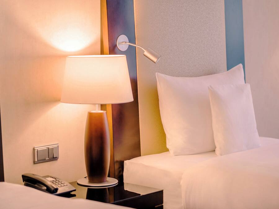 A hotel room with a bed, a bedside lamp, a telephone, and a wall-mounted light fixture.