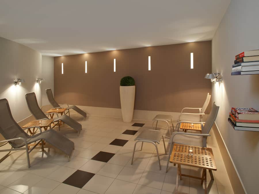 A modern lounge area with reclining chairs, a central planter, and a wall-mounted book shelf.