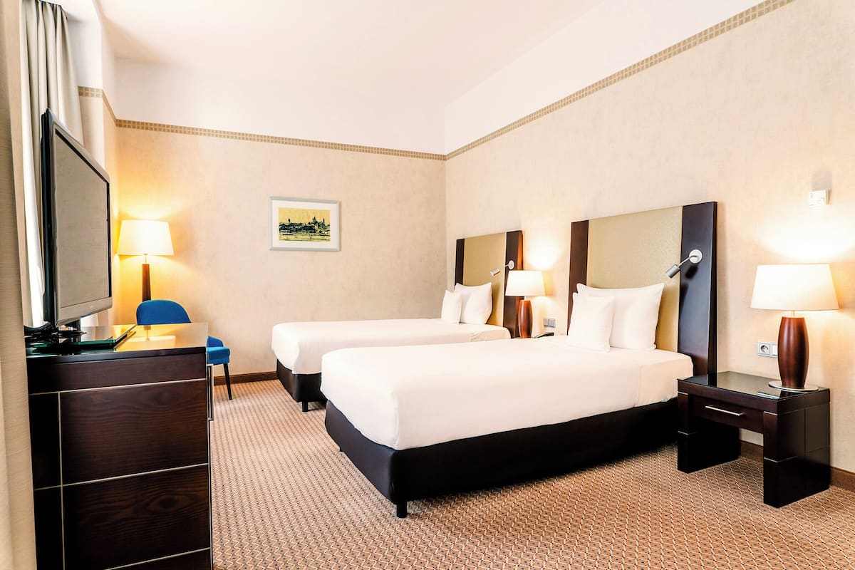 A hotel room with two beds, a desk, a chair, and a TV.