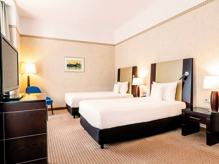 A hotel room with two beds, a desk, a chair, and a TV.
