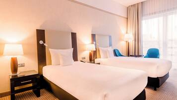 A hotel room with two beds, nightstands with lamps, a chair, and a large window with curtains.