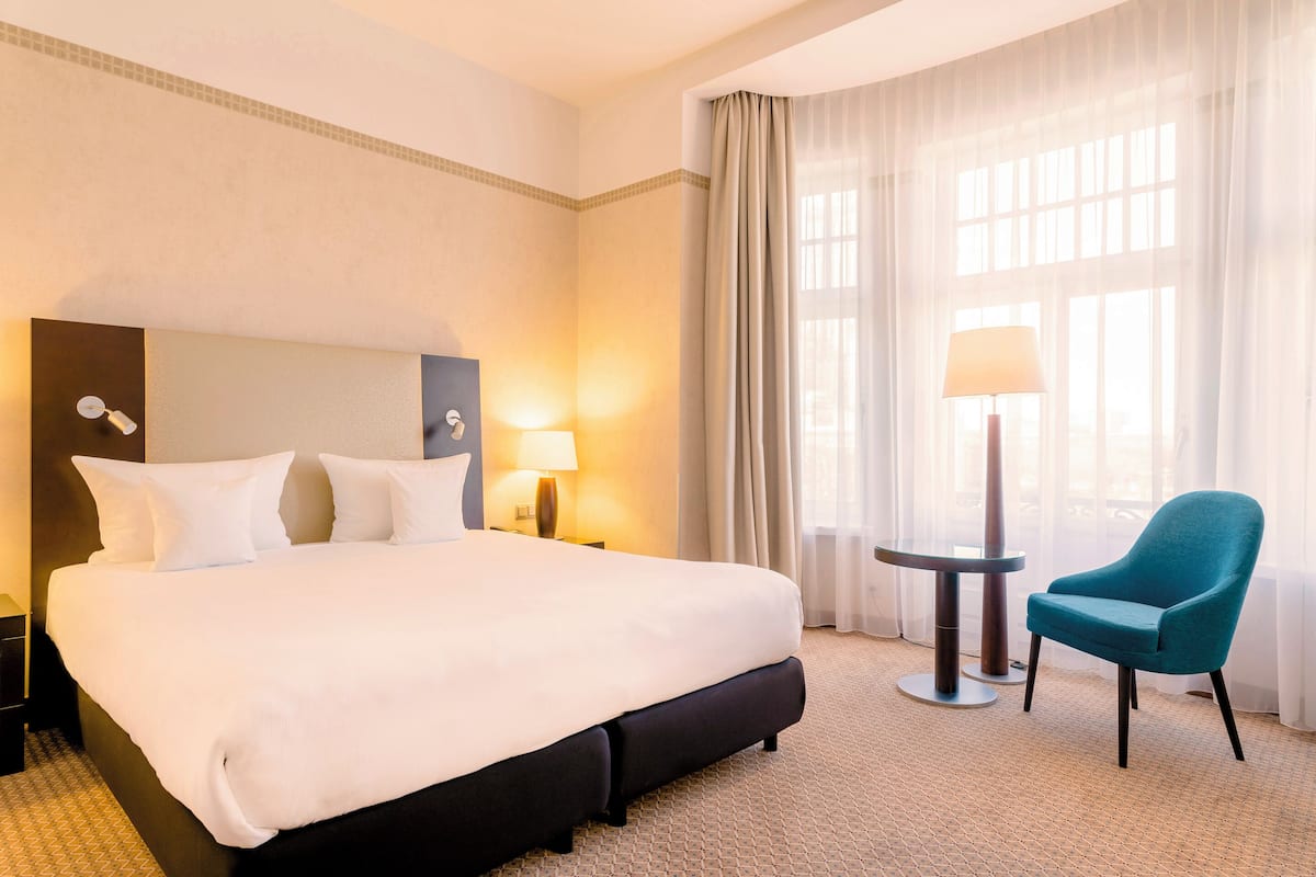 A hotel room with a large bed, a chair, a lamp, and a nightstand.