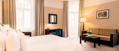 A hotel room with a large bed, a desk, a chair, a sofa, and a lamp.