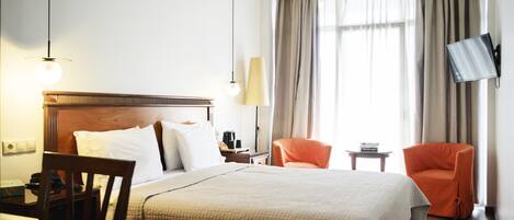 Ett hotellrum med en säng, ett skrivbord, en stol, en tv och ett fönster med gardiner.