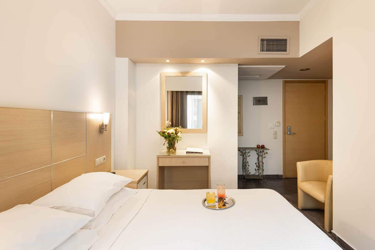 A hotel room with a large bed, a bedside table, a mirror, a small desk, a chair, and a tray with drinks.