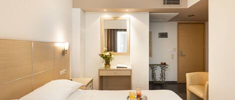 Habitación de hotel con una cama grande, una mesita de noche, un espejo, un escritorio pequeño, una silla y una bandeja con bebidas.