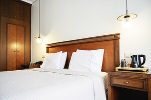 Habitación de hotel con cabecera de madera, ropa de cama blanca, una mesita de noche con cafetera y una lámpara.